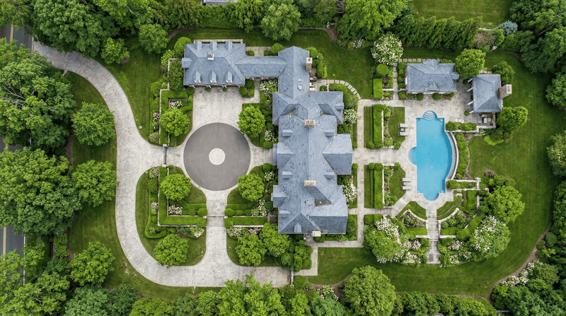 Aerial view of a large house with a pool surrounded by gardens and trees.