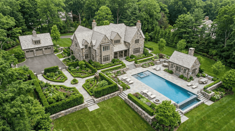 Aerial view of a large stone mansion with a pool and well-manicured gardens.